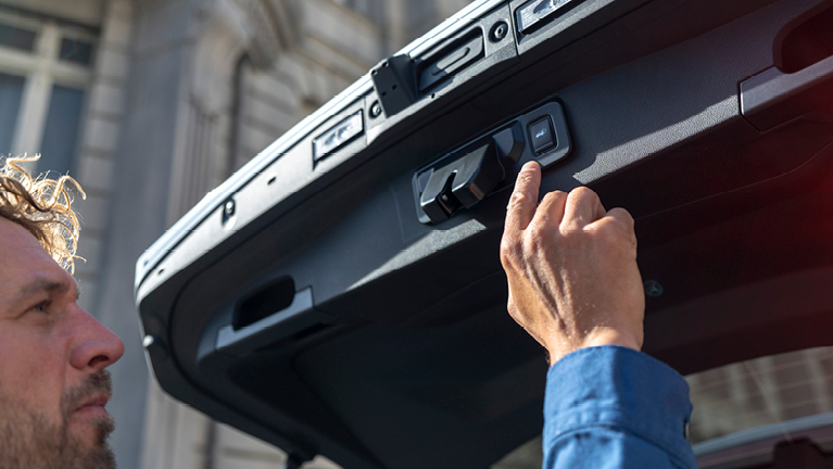 Mann in blauem Hemd öffnet Kofferraum, Nahaufnahme der Hand am Verriegelungsmechanismus