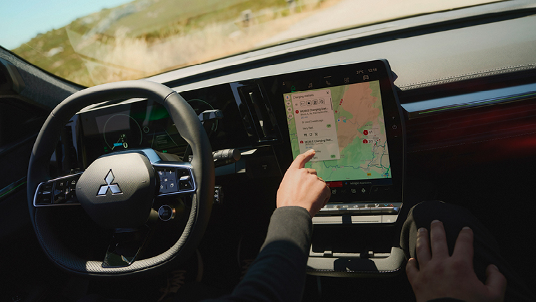 Fahrer/in bedient den zentralen Touchscreen-Bildschirm des Mitsubishi Eclipse Cross Diamant PLUS mit aktiver Navigationsansicht